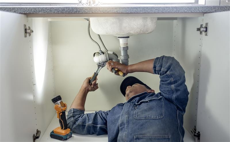 Plumber repairing pipes beneath a bathroom sink in West Palm Beach