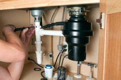 Plumber repairing a garbage disposal beneath a kitchen sink in West Palm Beach