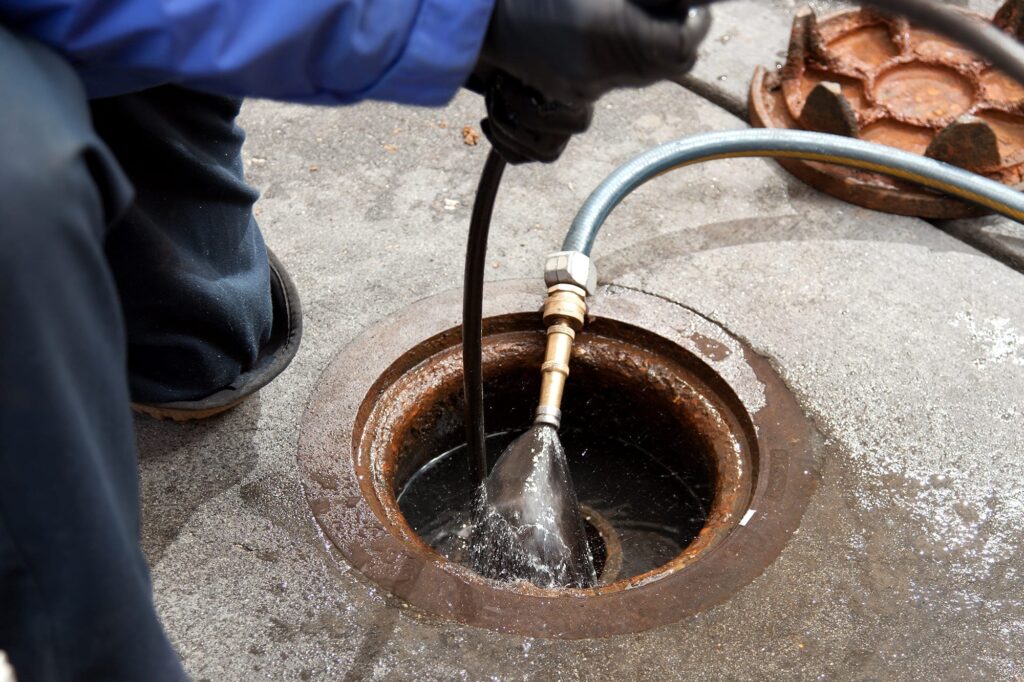Plumber hydro jetting a sewer line through a manhole in West Palm Beach