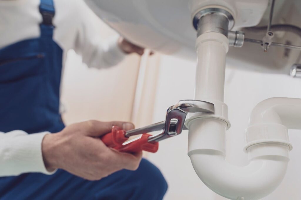 Plumber repairing a white drain pipe beneath a sink in West Palm Beach