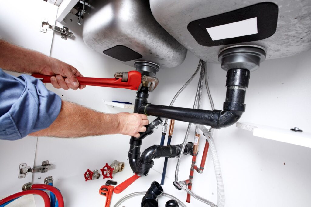 Plumber repairing drain pipes beneath a kitchen sink in West Palm Beach